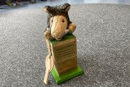 Ein aus Holz gefertigter Wanderpokal. Er besteht aus einem Quader an auf dessen Spitze ein Tier mit dem Namen Rudi sitzt.