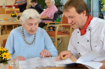 Seniorin und Koch sprechen über ausgebreiteten Speiseplan